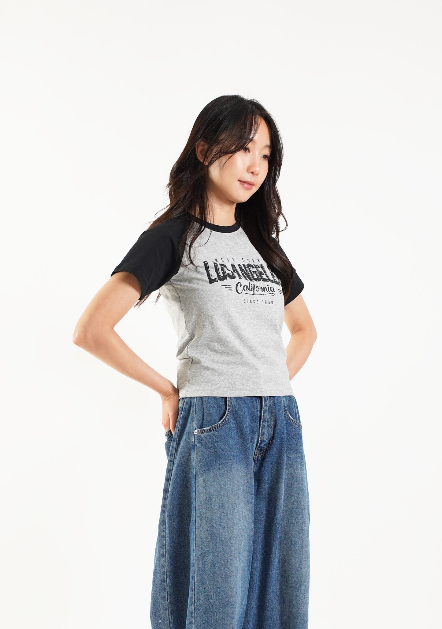 Person wearing a black and gray t-shirt with blue jeans standing against a white backdrop
