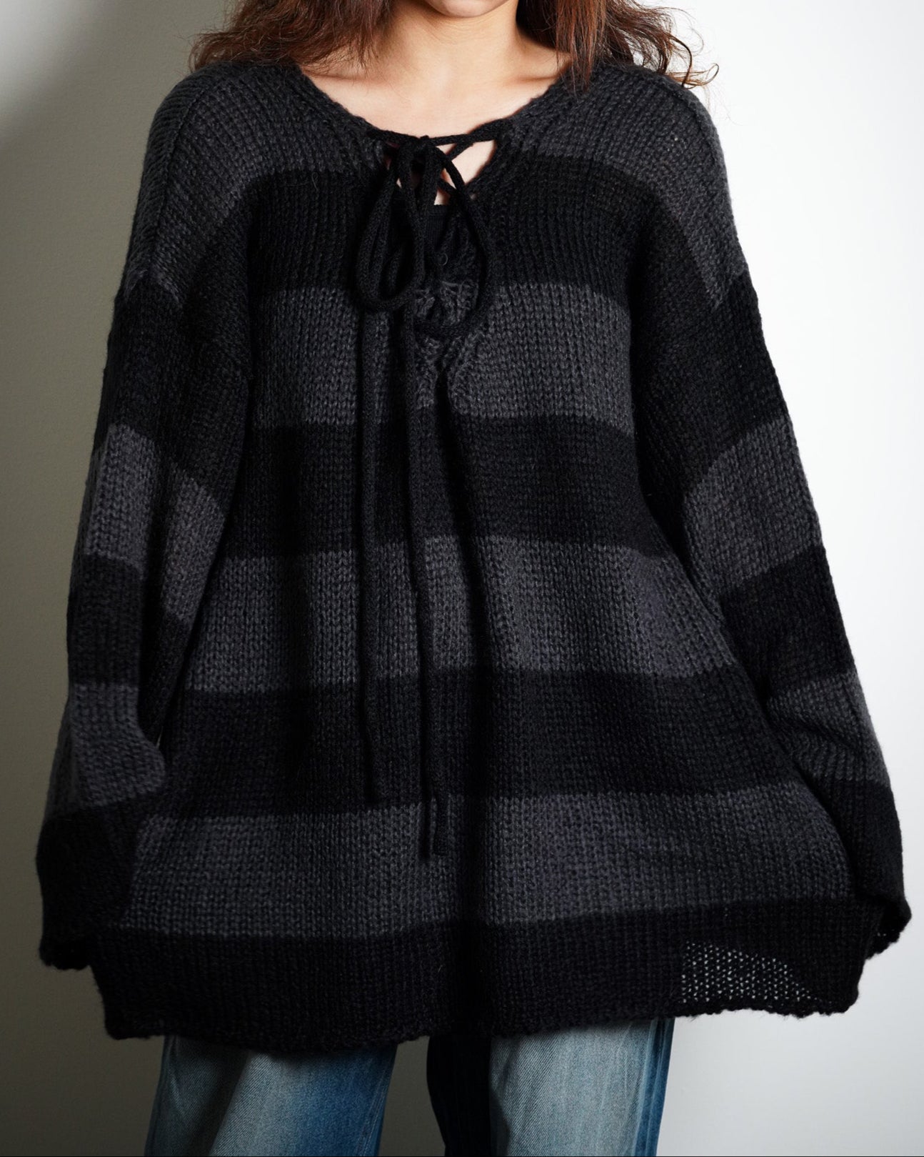 Person wearing a black and gray striped poncho with a leopard print hat on a plain background